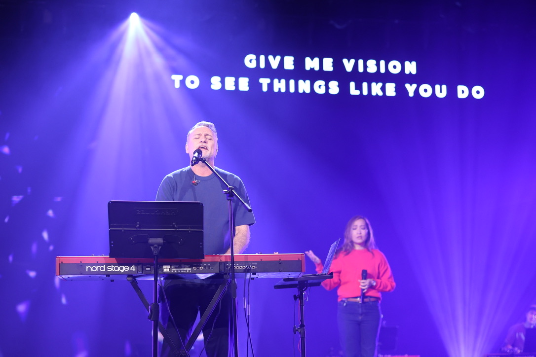 Mark singing at the keyboard under purple stage lighting