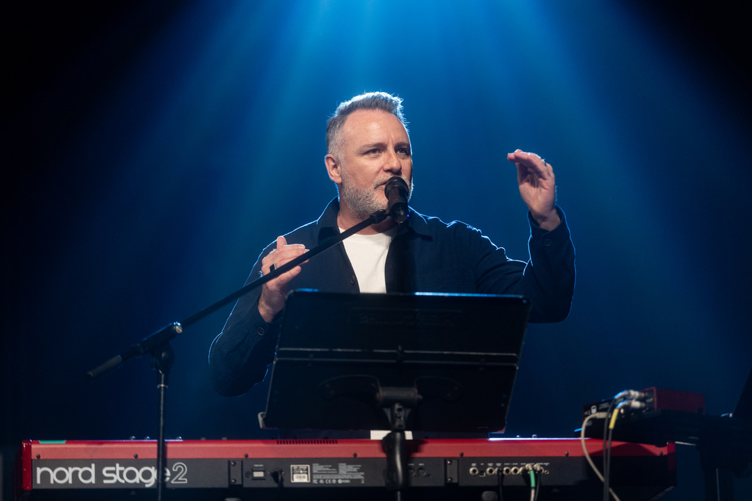 Mark Stevens speaking at a microphone behind a keyboard
